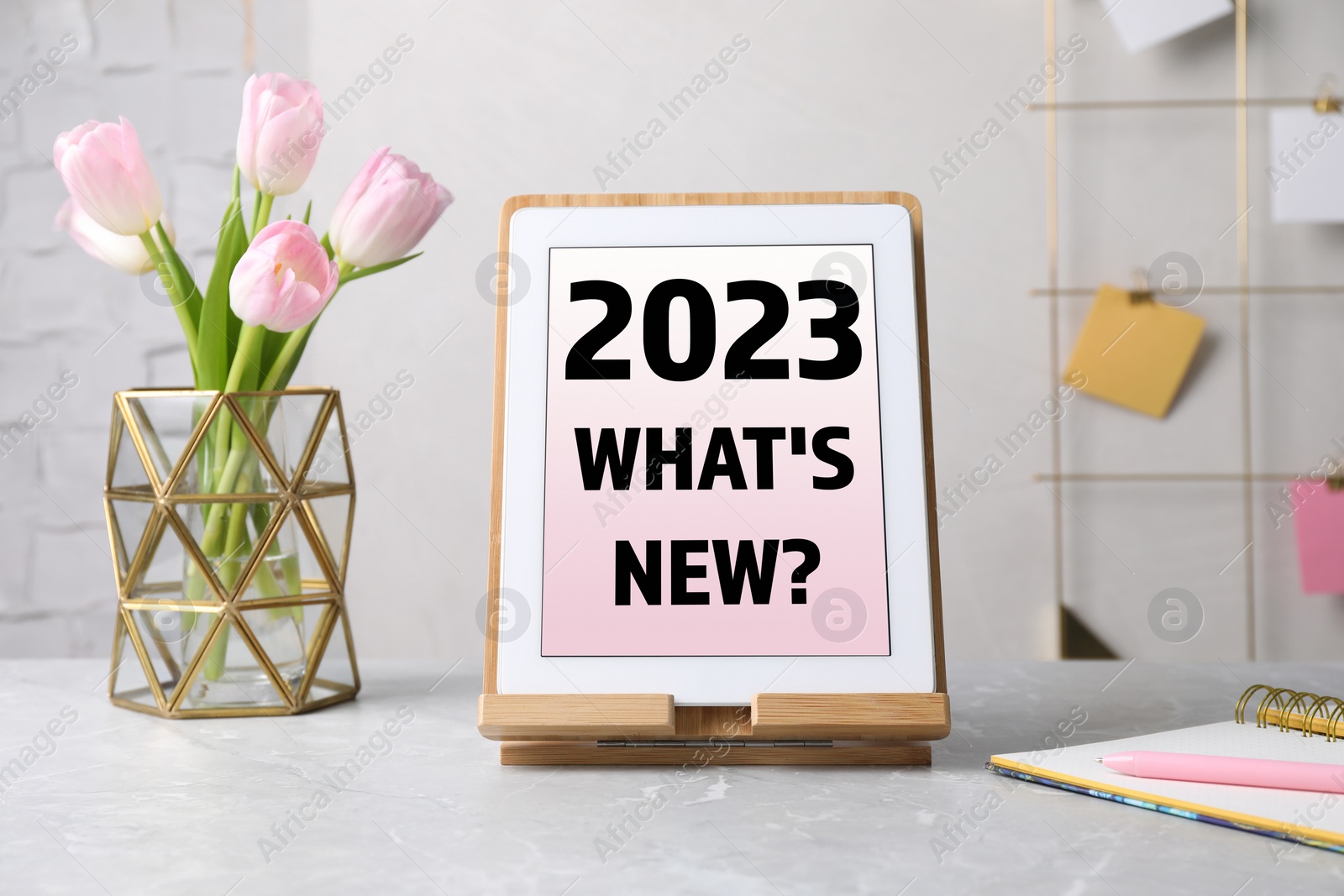 Image of Future trends. 2023 What's New? text on tablet display. Modern gadget, flowers and stationery on table