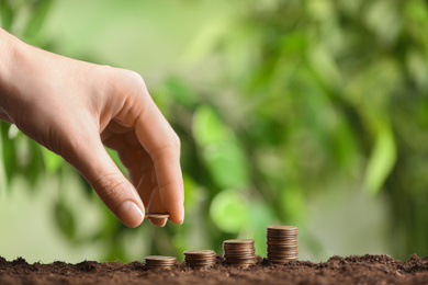 Woman stacking coins on soil against blurred background, closeup. Money savings