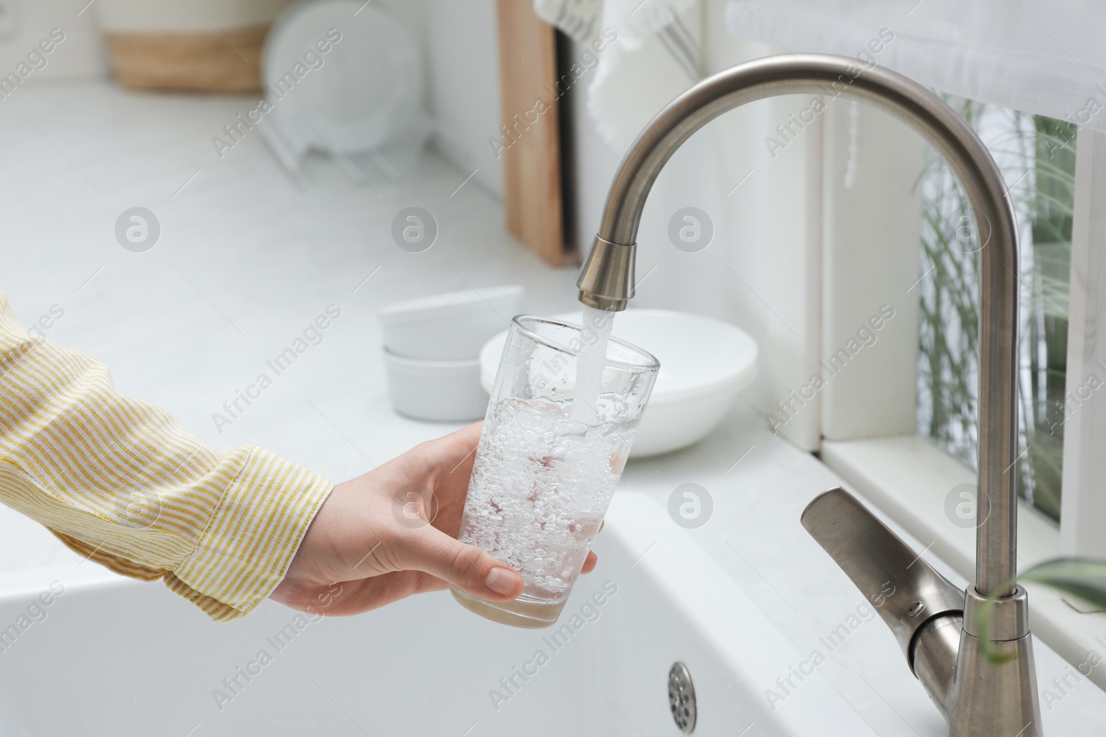 Photo of Woman filling glass with water from tap in kitchen, closeup