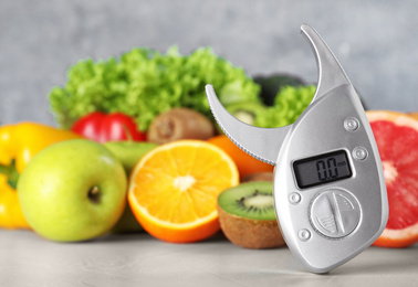 Photo of Digital body fat caliper, vegetables and fruits on table. Diet plan from nutritionist