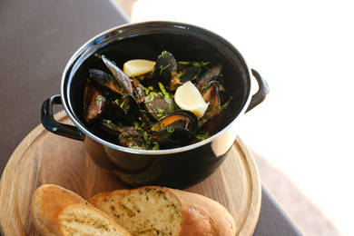 Mussels with lemon slices in pot on wooden board