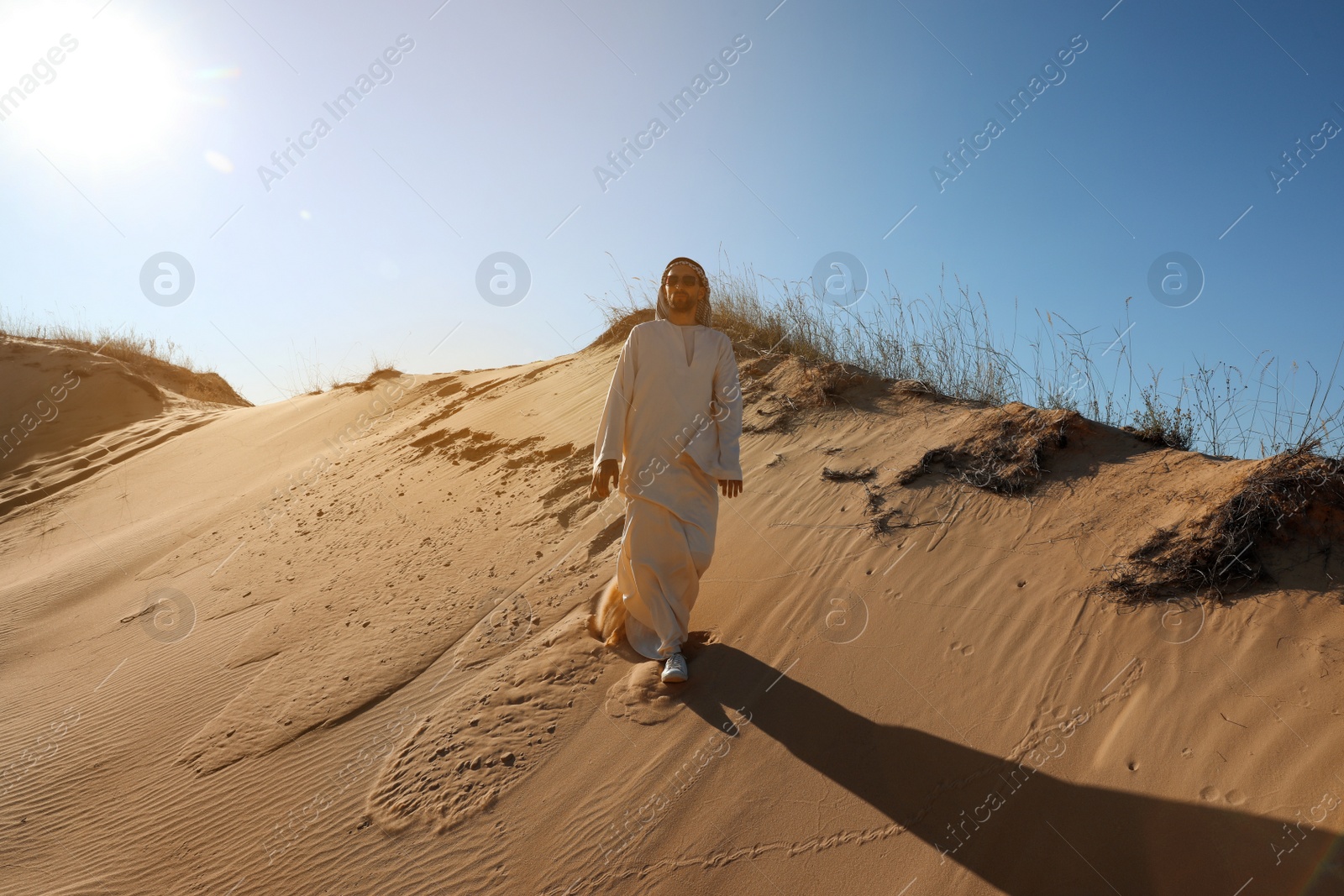 Photo of Man in arabic clothes walking through desert on sunny day