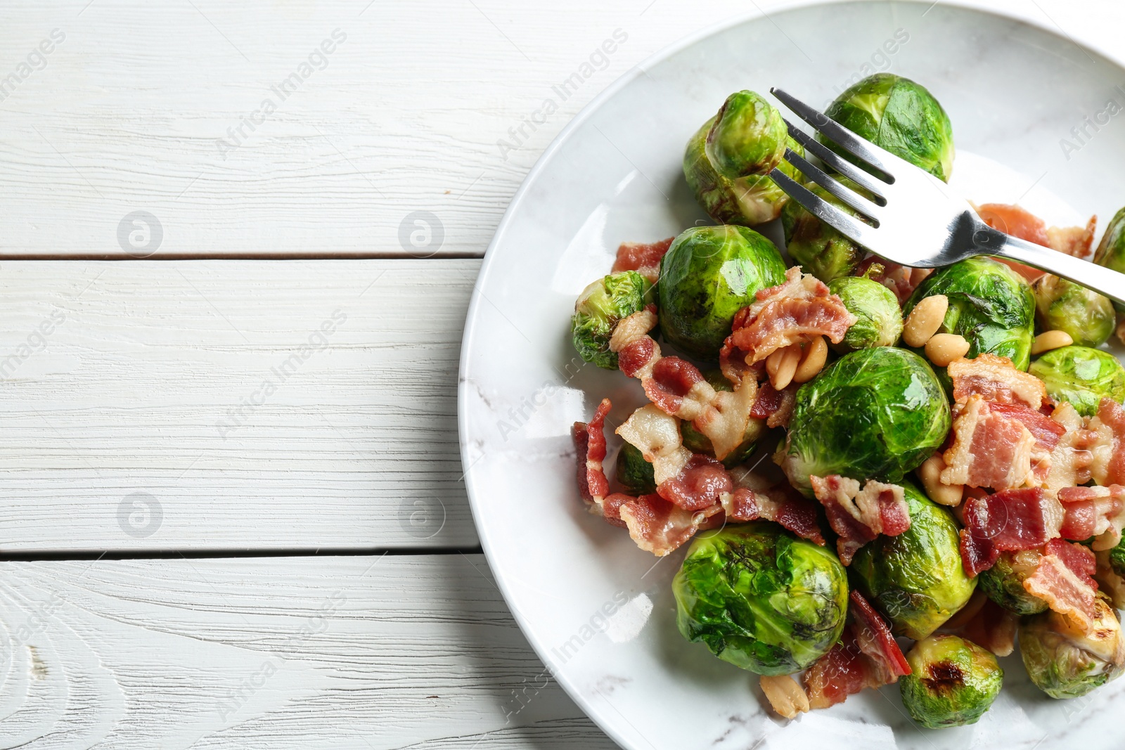 Photo of Delicious Brussels sprouts with bacon on white wooden table, top view. Space for text