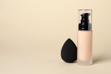 Photo of Bottle of skin foundation and sponge on beige background, space for text. Makeup product