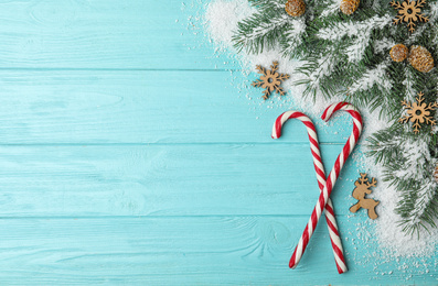 Photo of Flat lay composition with candy canes, fir branches and snow on light blue wooden background, space for text. Winter holidays