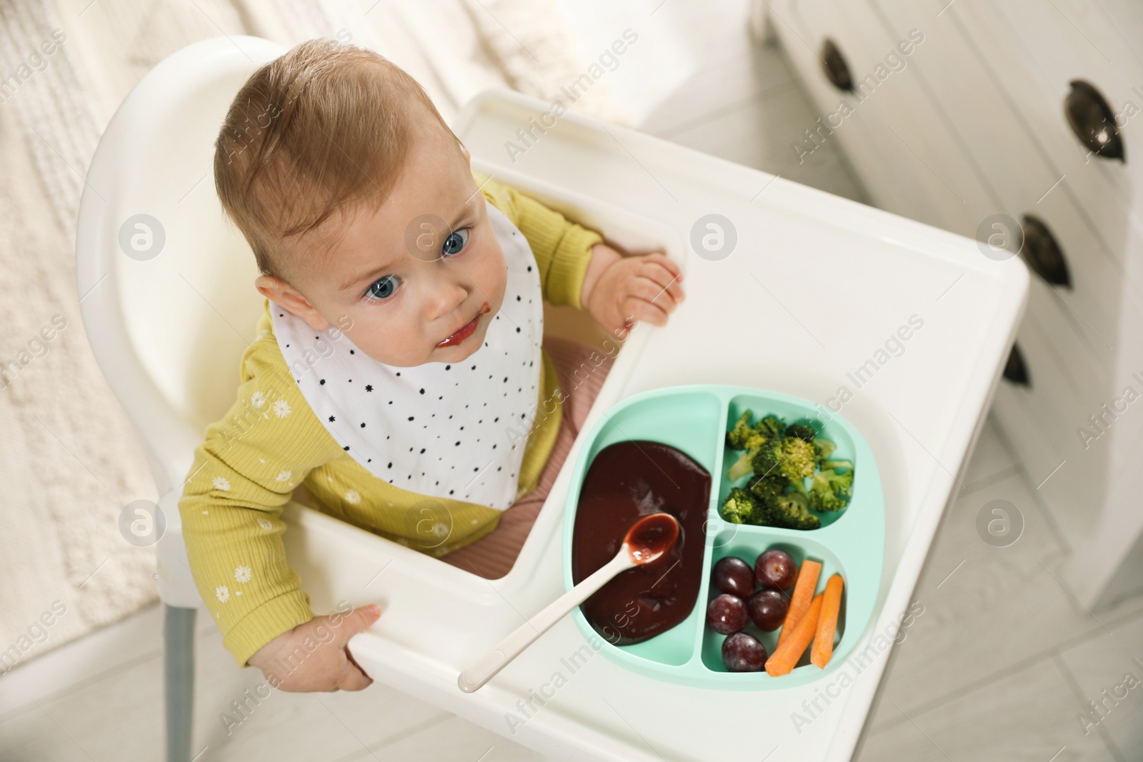 Photo of Cute little baby wearing bib while eating at home, above view