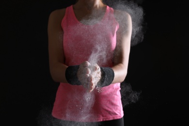Photo of Young woman applying chalk powder on hands against dark background