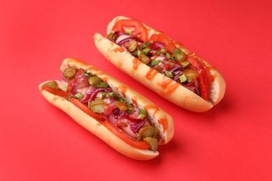 Photo of Tasty hot dogs with onion, tomato, pickles and sauce on red background