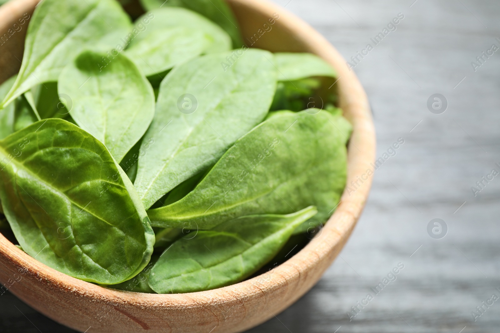 Photo of Bowl of fresh green healthy spinach on dark wooden table, closeup