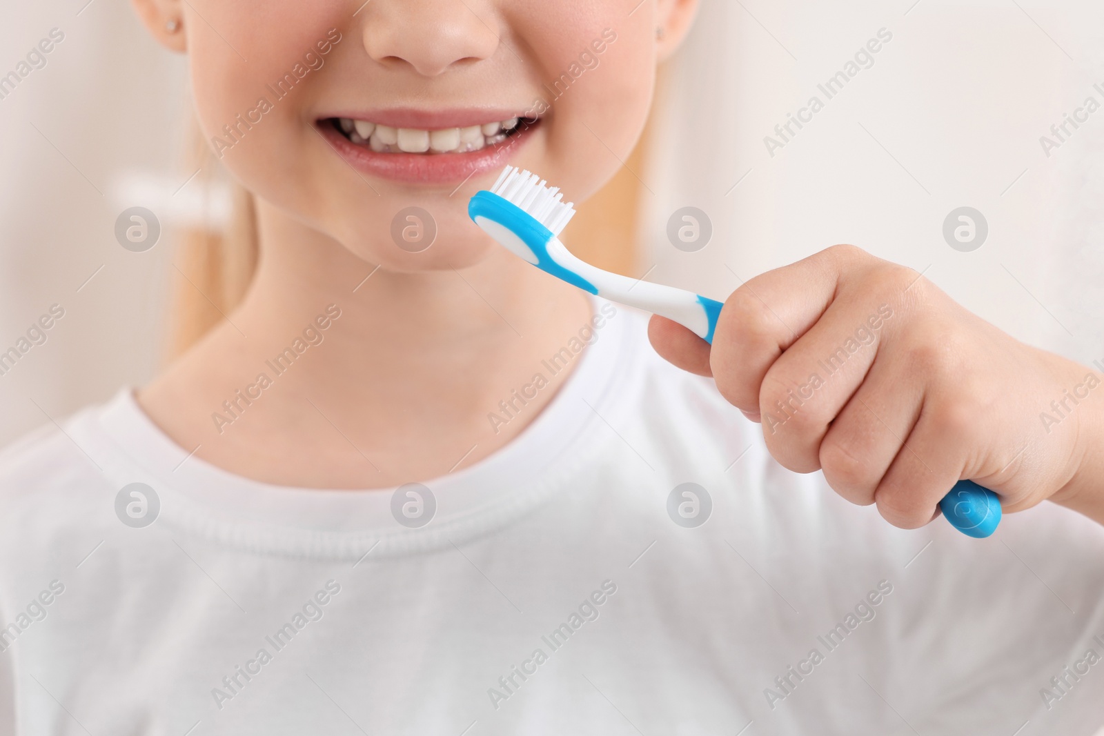 Photo of Little girl holding plastic toothbrush indoors, closeup