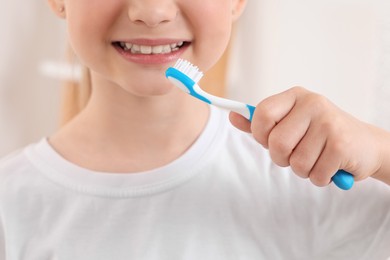 Photo of Little girl holding plastic toothbrush indoors, closeup