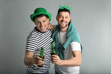 Photo of Happy men in St Patrick's Day outfits with beer on light grey background