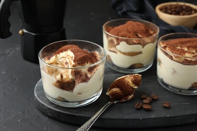 Photo of Delicious tiramisu in glasses, spoon and coffee beans on black table