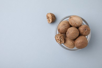 Photo of Nutmegs in glass bowl on white background, top view. Space for text