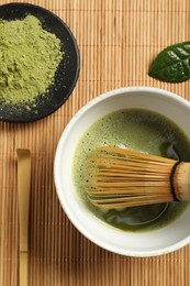 Photo of Cup of fresh matcha tea with whisk, spoon and green powder on bamboo mat, flat lay