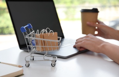 Internet shopping. Small cart with bags near woman using laptop indoors