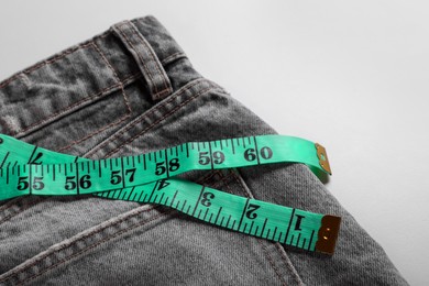 Photo of Jeans with measuring tape on light grey background, closeup. Weight loss concept