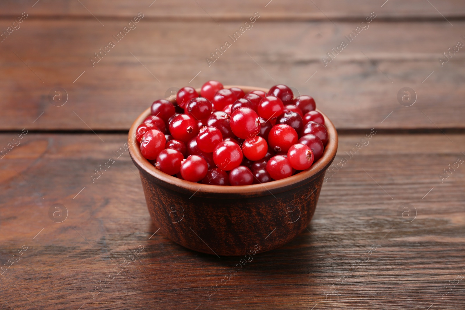 Photo of Fresh ripe cranberries in bowl on wooden table