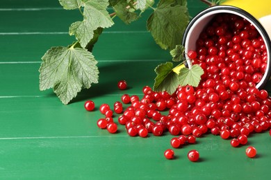 Photo of Many ripe red currants, mug and leaves on green wooden table. Space for text