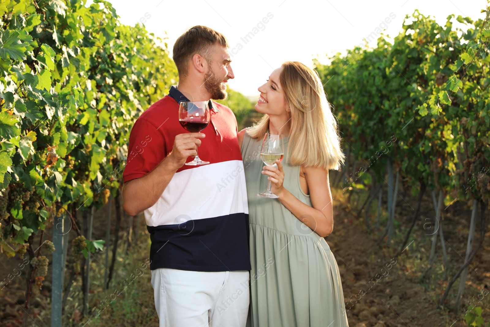 Photo of Young couple holding glasses of wine at vineyard