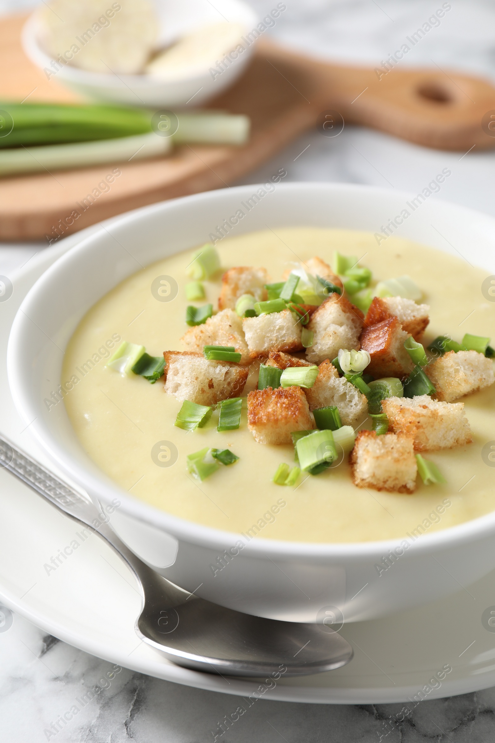 Photo of Tasty potato soup with croutons in bowl and spoon on white marble table, closeup