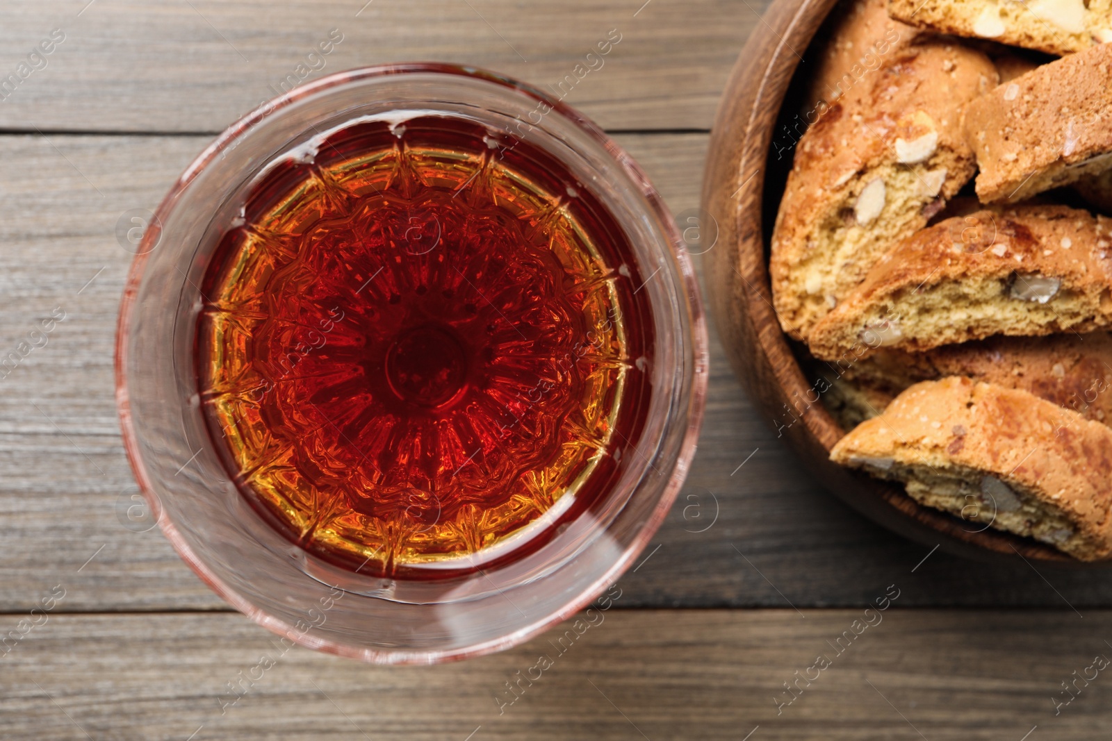 Photo of Tasty cantucci and glass of liqueur on wooden table, flat lay. Traditional Italian almond biscuits