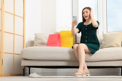 Special Promotion. Emotional woman looking at smartphone on sofa indoors. Space for text