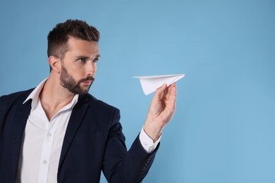 Handsome businessman playing with paper plane on light blue background. Space for text