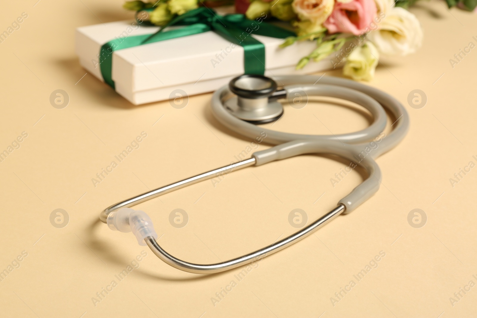 Photo of Stethoscope, gift box and eustoma flowers on beige background. Happy Doctor's Day