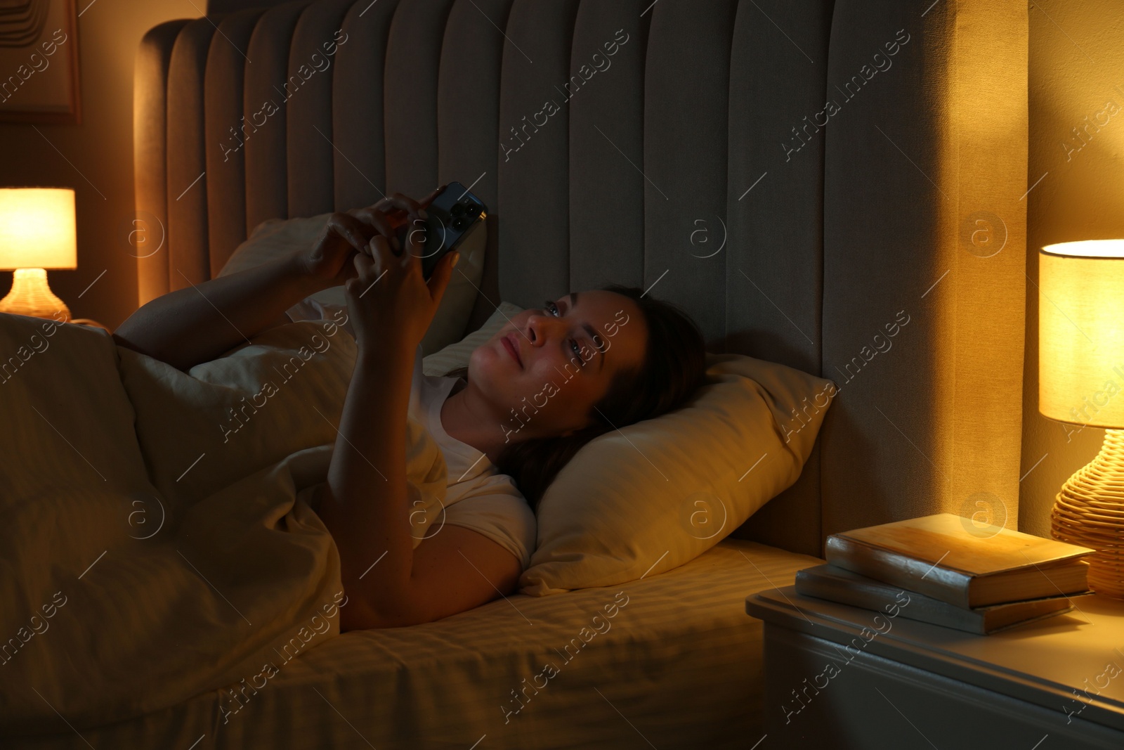 Photo of Woman using smartphone in bed at night. Internet addiction