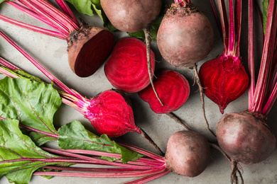 Photo of Cut and whole raw beets on light grey table, flat lay
