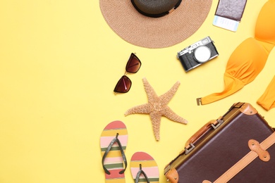 Photo of Flat lay composition with suitcase and beach objects on yellow background