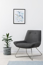 Photo of Comfortable armchair and houseplant near white wall indoors. Interior design