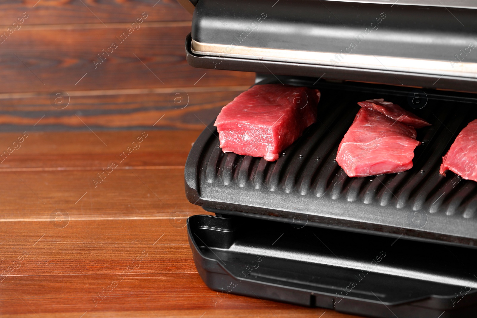 Photo of Electric grill with raw meat on wooden table, space for text