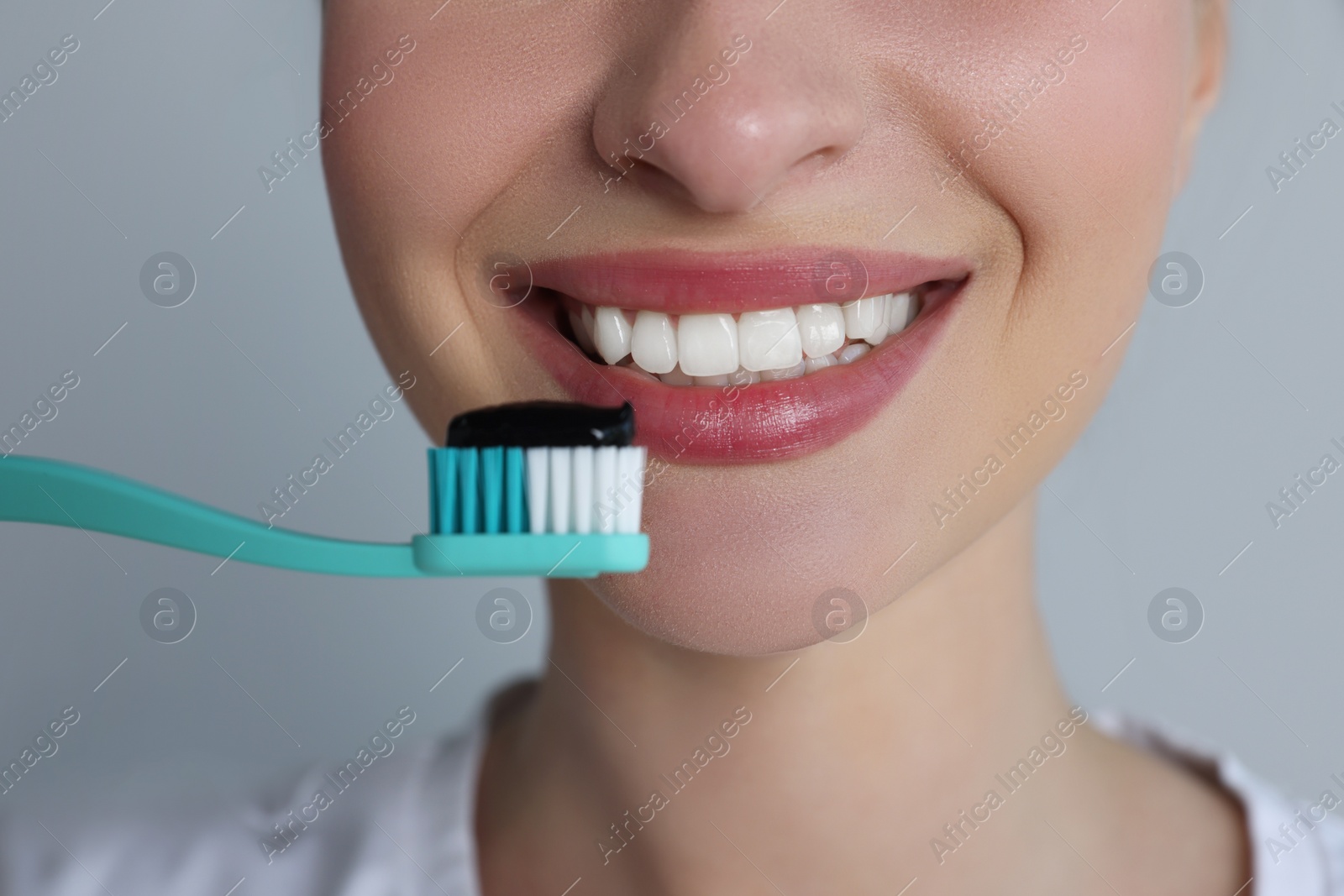 Photo of Woman holding toothbrush with charcoal toothpaste on grey background, closeup