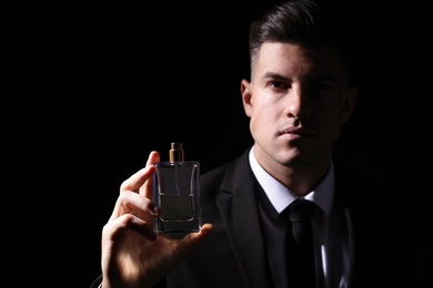 Photo of Man with luxury perfume against black background, focus on bottle