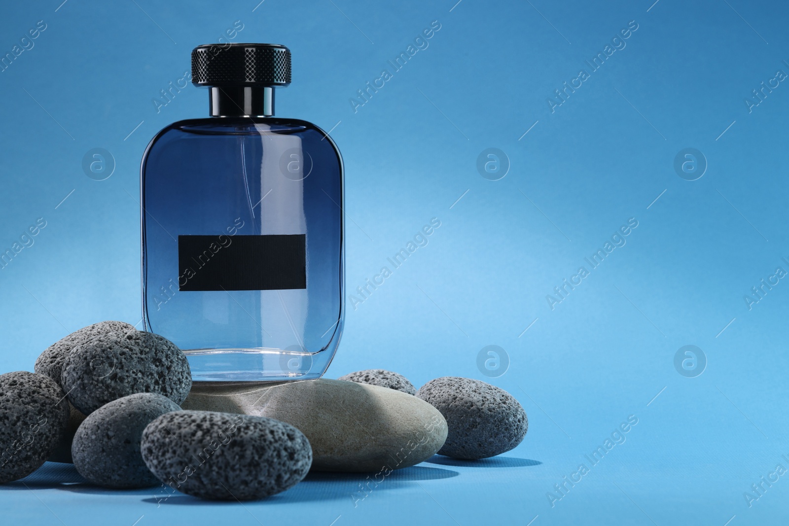 Photo of Stylish presentation of luxury men`s perfume on stones against light blue background. Space for text