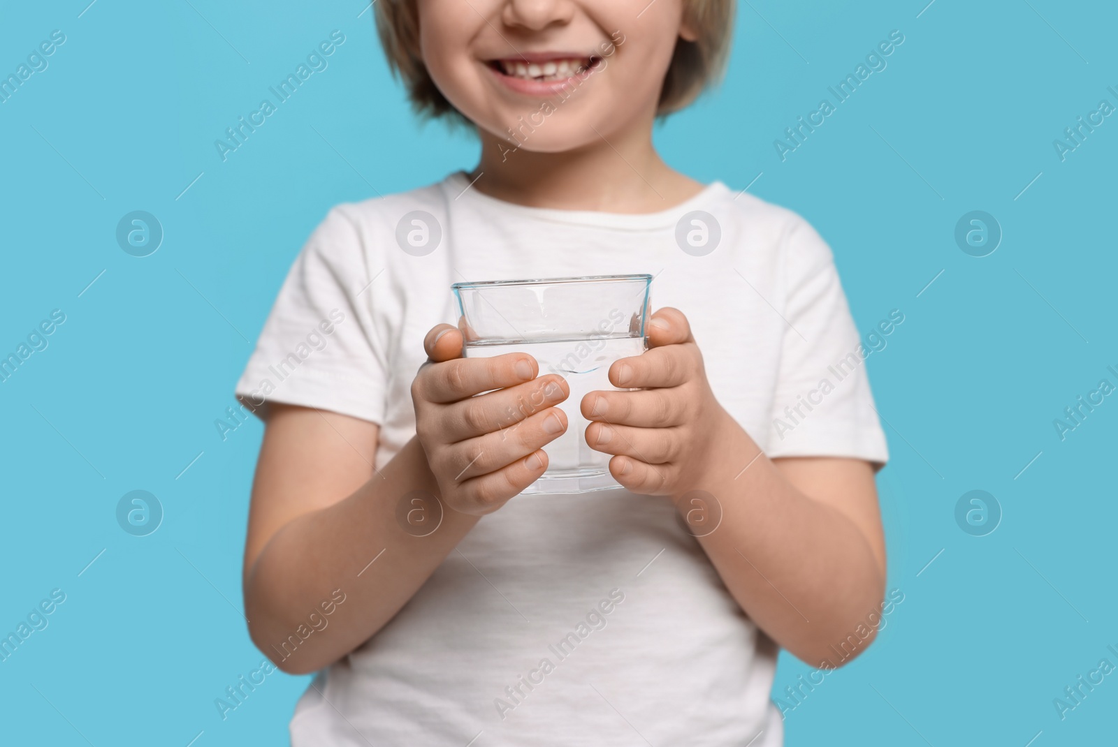Photo of Little boy holding glass of fresh water on light blue background, closeup
