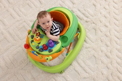 Photo of Cute baby making first steps with toy walker on soft carpet, above view. Space for text