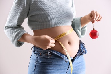 Photo of Woman with Christmas ball and measuring tape on white background, closeup. Overweight problem after New Year party
