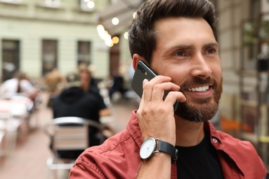 Photo of Handsome man talking on smartphone while walking outdoors, space for text