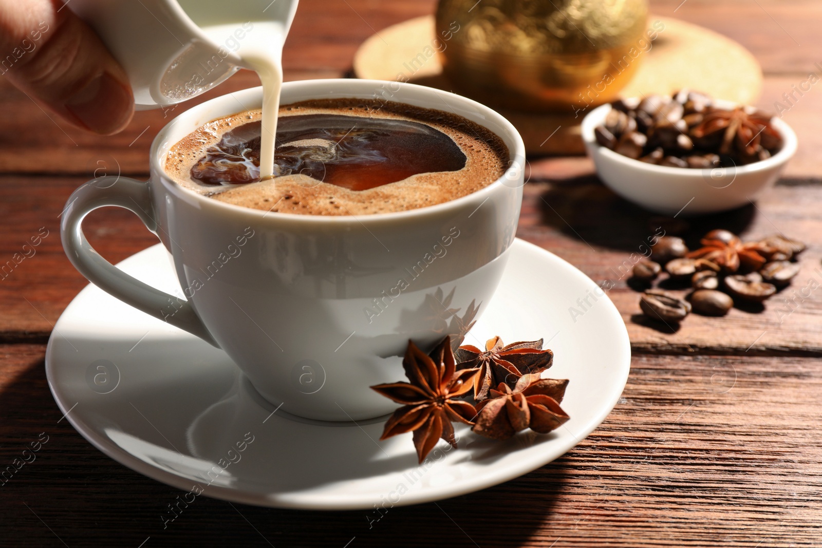 Photo of Woman pouring milk into cup of coffee with anise stars at wooden table