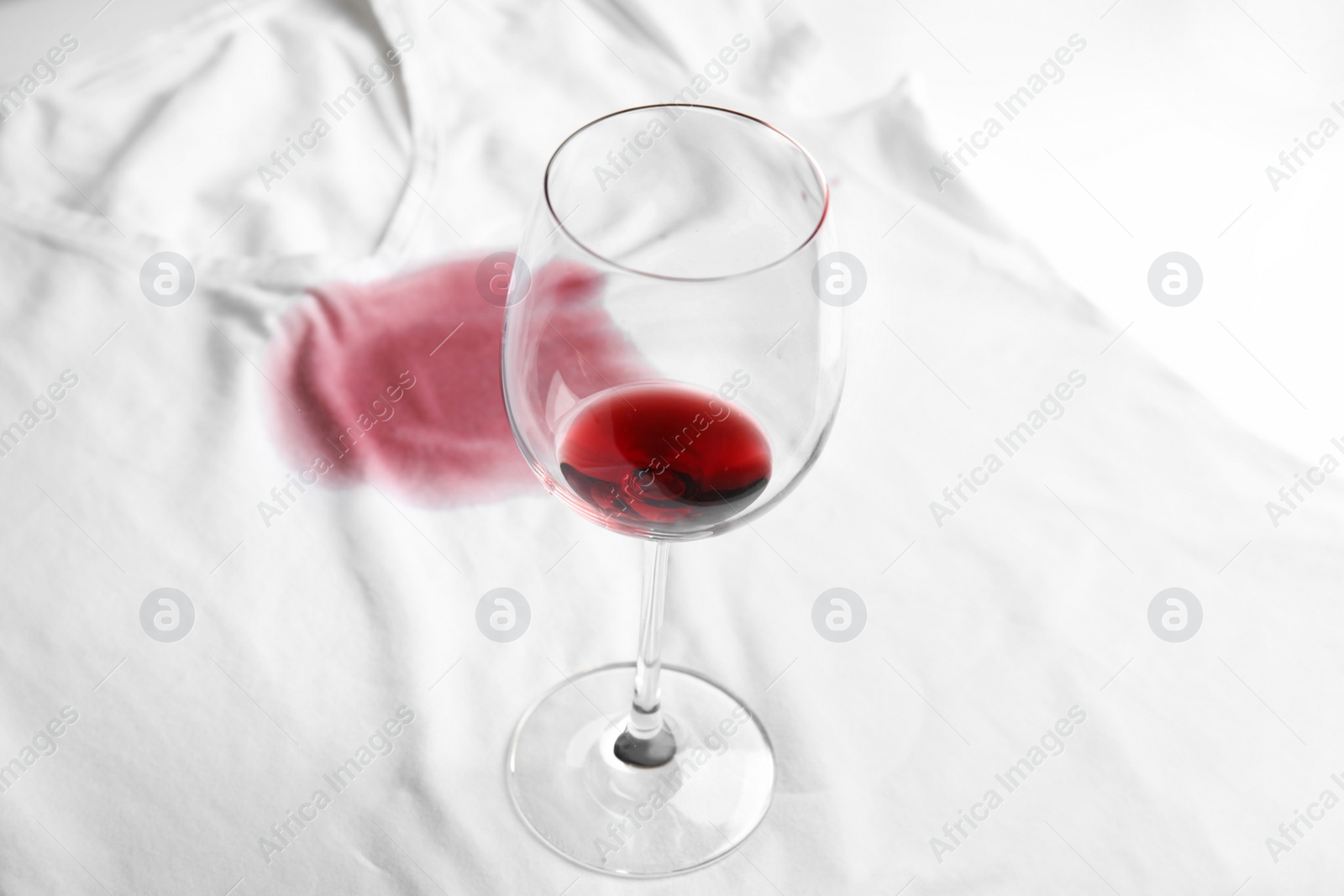 Photo of Transparent glass and spilled exquisite red wine on white t-shirt