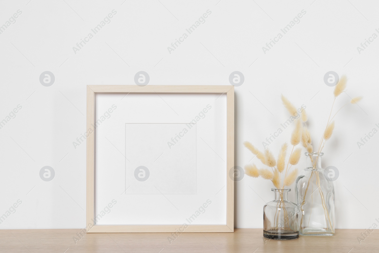 Photo of Empty photo frame and vases with dry decorative spikes on wooden table. Mockup for design