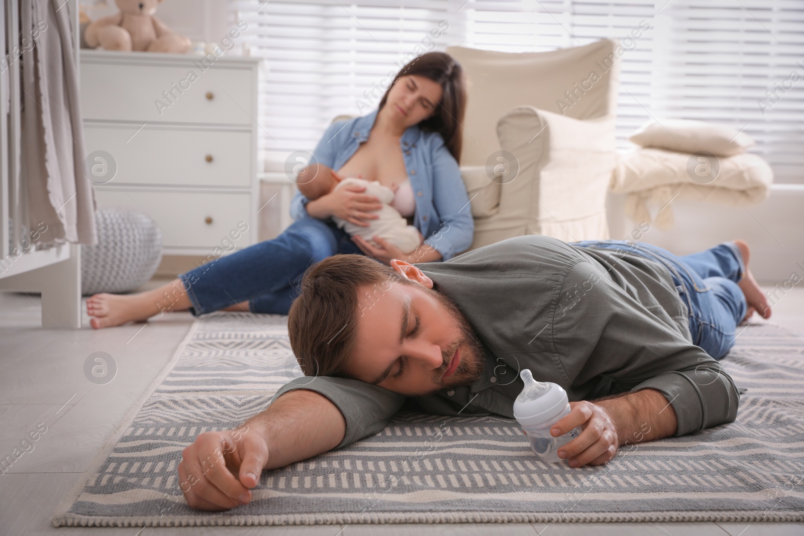 Photo of Tired young parents with their baby sleeping on floor in children's room