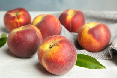 Fresh juicy peaches, leaves and fabric on white wooden table