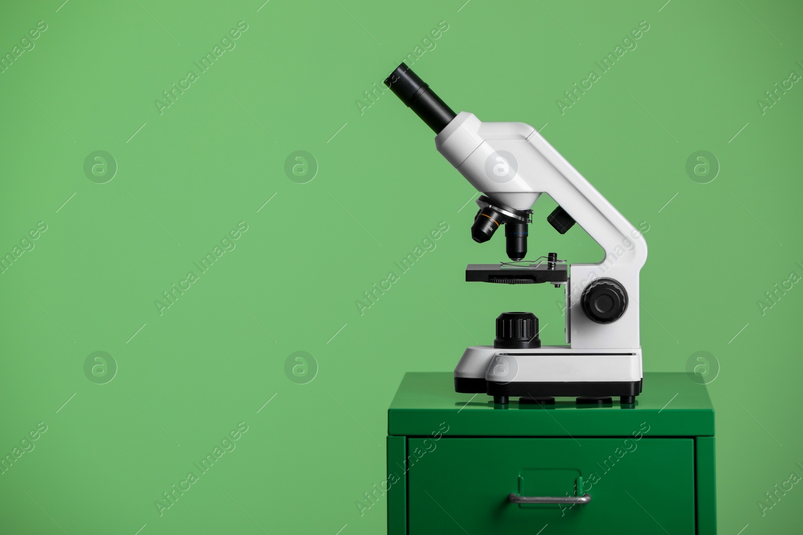 Photo of Modern medical microscope on lab drawer against green background, space for text
