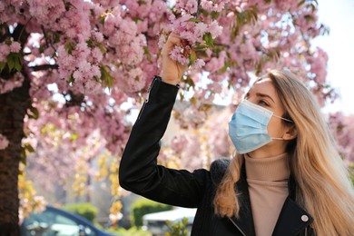 Photo of Woman with protective mask near blossoming tree outdoors. Seasonal pollen allergy