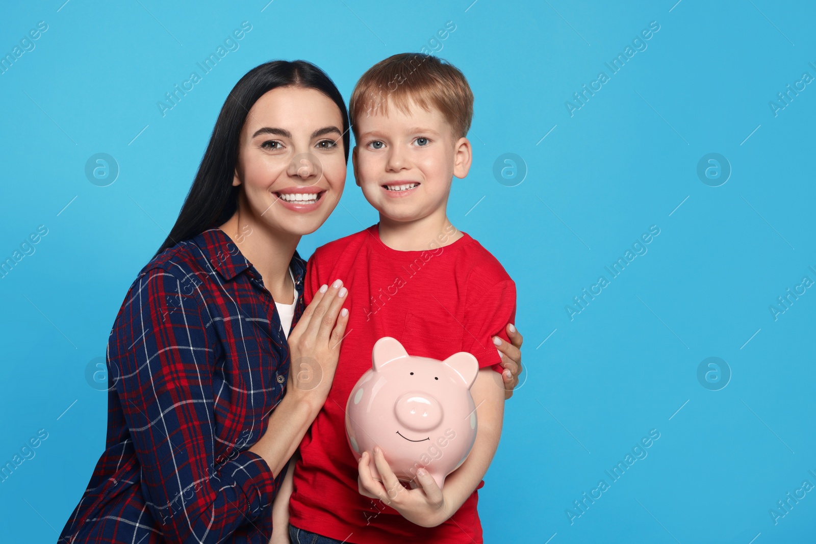 Photo of Mother and her son with ceramic piggy bank on light blue background