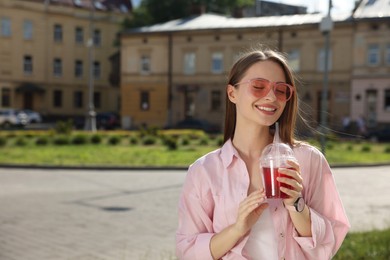 Young woman in sunglasses with plastic cup of fresh juice on city street, space for text